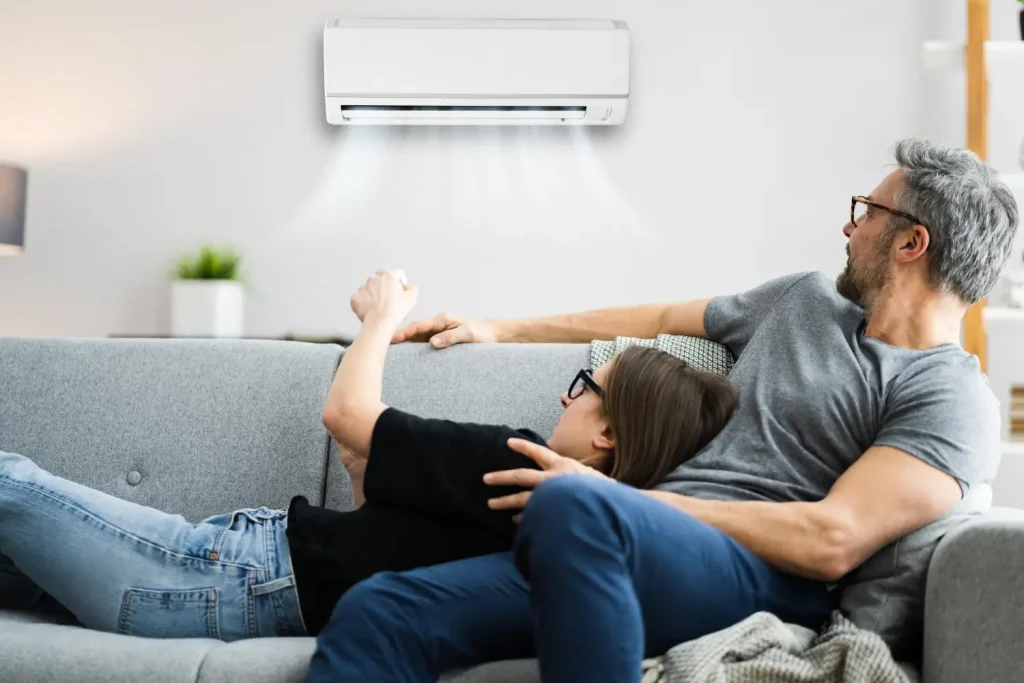 A couple relaxing on a couch under a wall-mounted air conditioning unit.