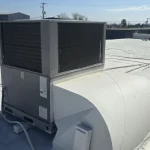 Rooftop HVAC unit installed on a flat roof in a commercial area under a sunny sky.