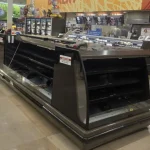 Empty commercial refrigeration display case in a grocery store under maintenance.