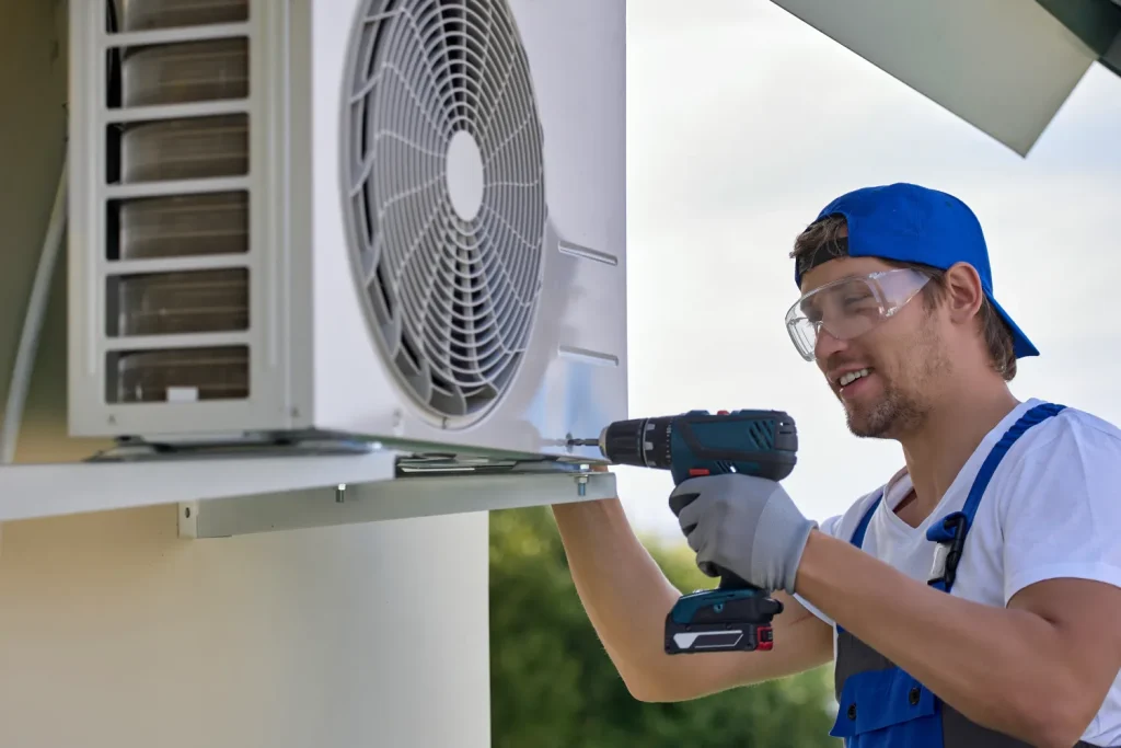 Technician repairing an outdoor air conditioning unit with a drill.