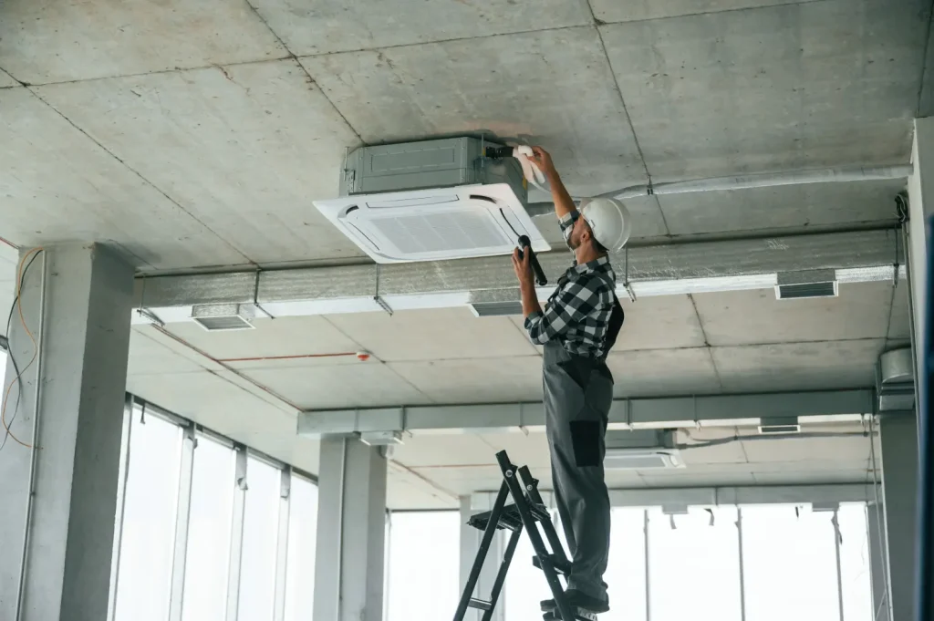 Technician performing routine maintenance on a ceiling-mounted air conditioning unit.