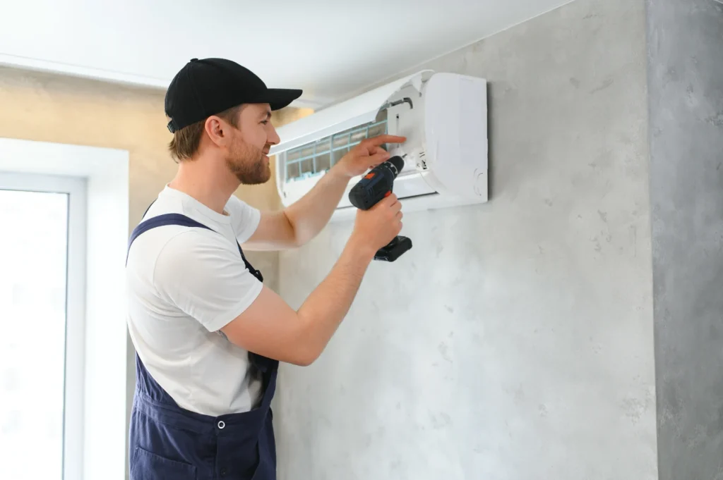 Technician servicing a wall-mounted air conditioning unit with a drill.